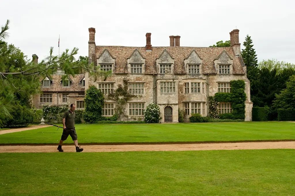 A gardener walking in front of a historic manor house