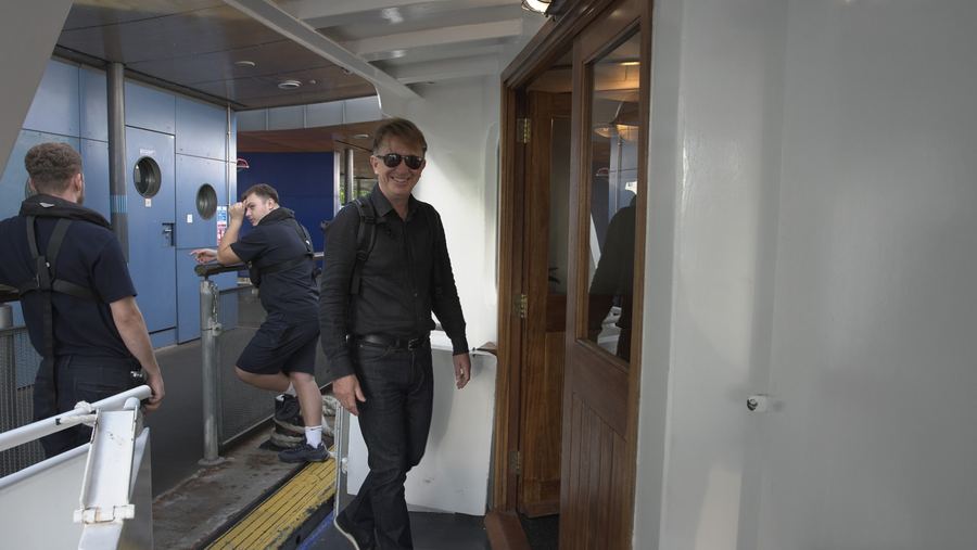 A guest in sunglasses and a black shirt smiles as he steps aboard