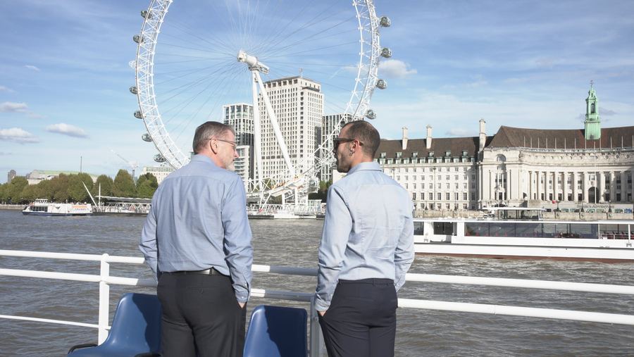 Two guests in blue shirts look out over the Thames towards the London Eye and County Hall