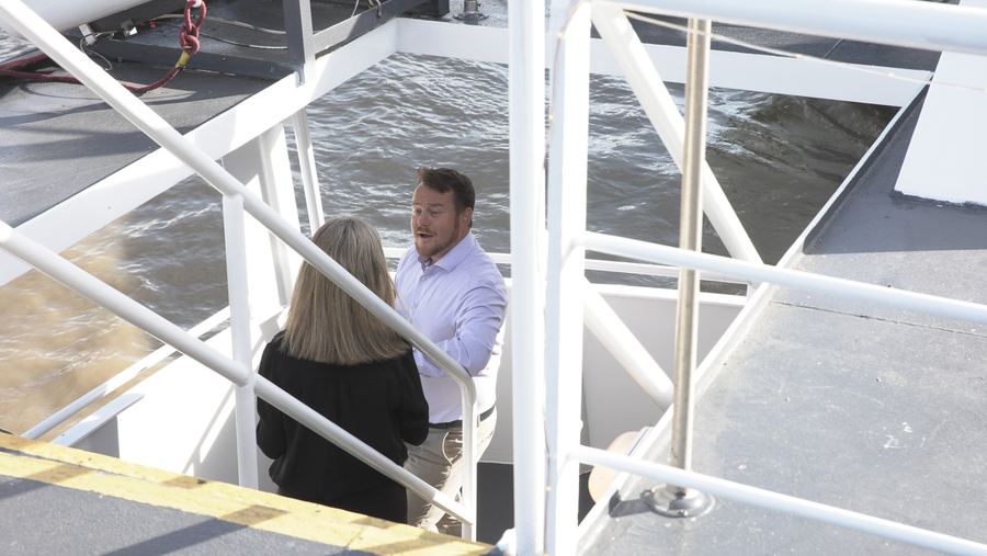 A guest in a lilac shirt chats with a colleague on the stairs above the water, seen from the upper deck