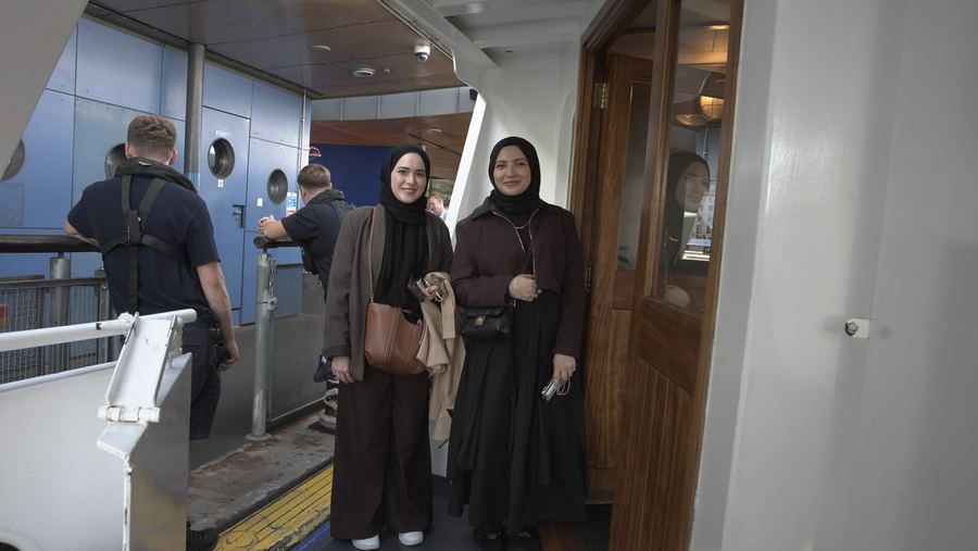 Two guests in headscarves and smart jackets smile for the camera at the boarding point